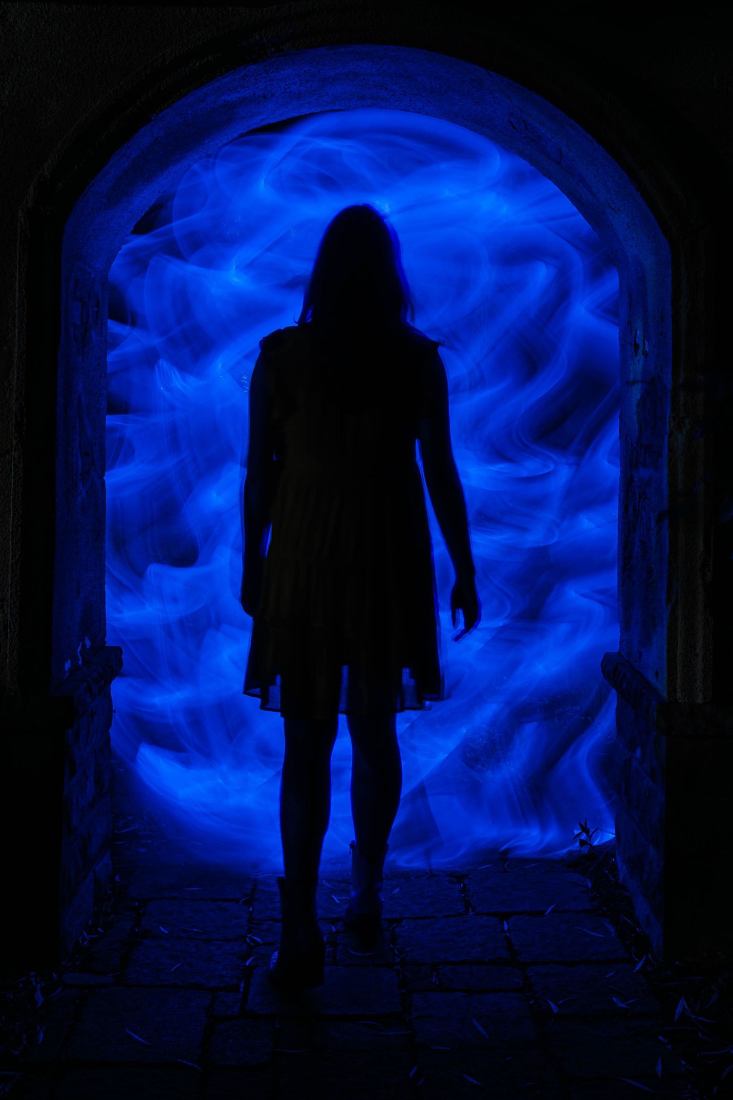 Silhouette stands in blue-lit archway creating mysterious atmosphere.