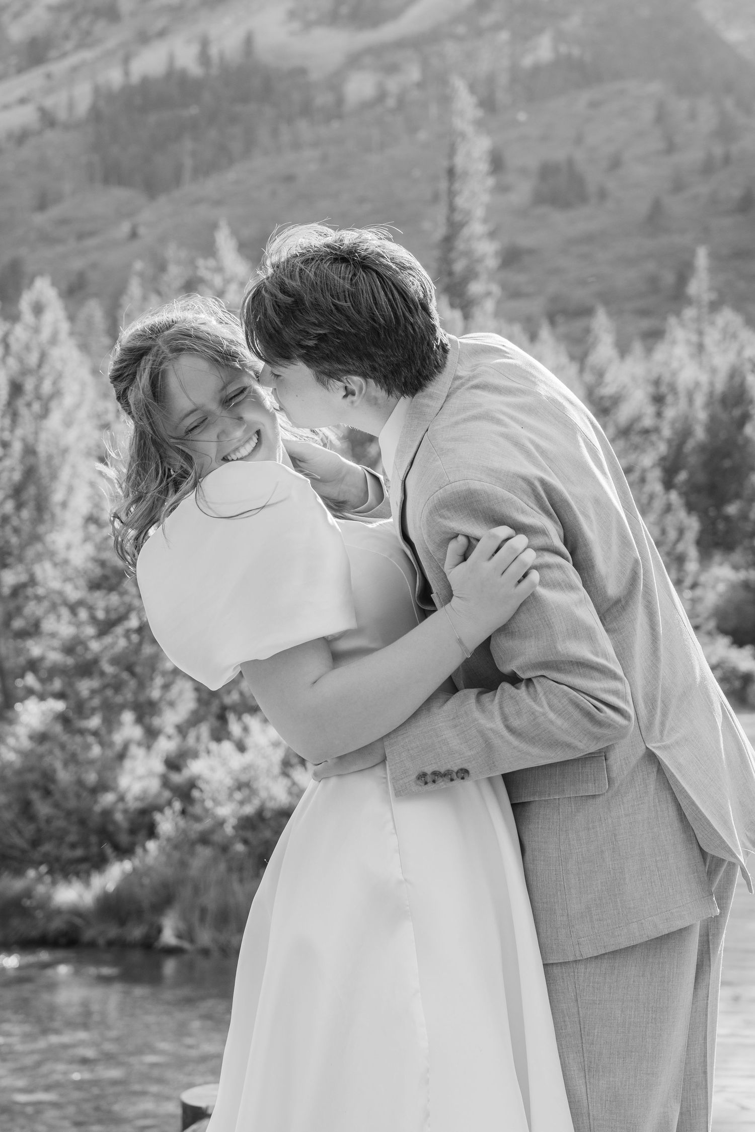 A joyful wedding moment captured in black and white as a couple shares a laugh on a mountain boardwalk.