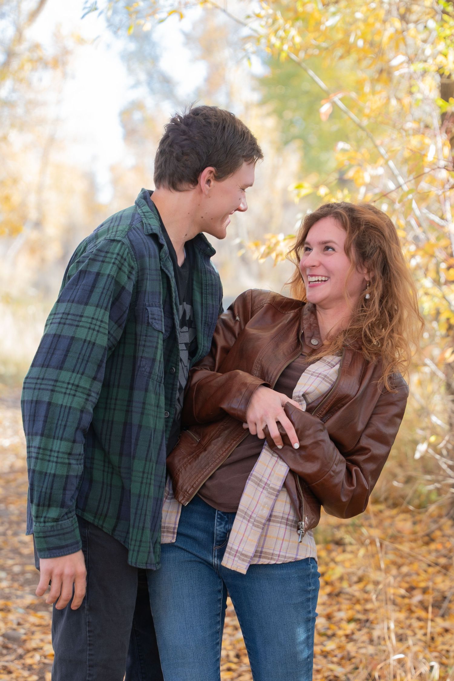 A playful autumn photoshoot showing a couple in plaid and leather jackets laughing together among fall foliage.