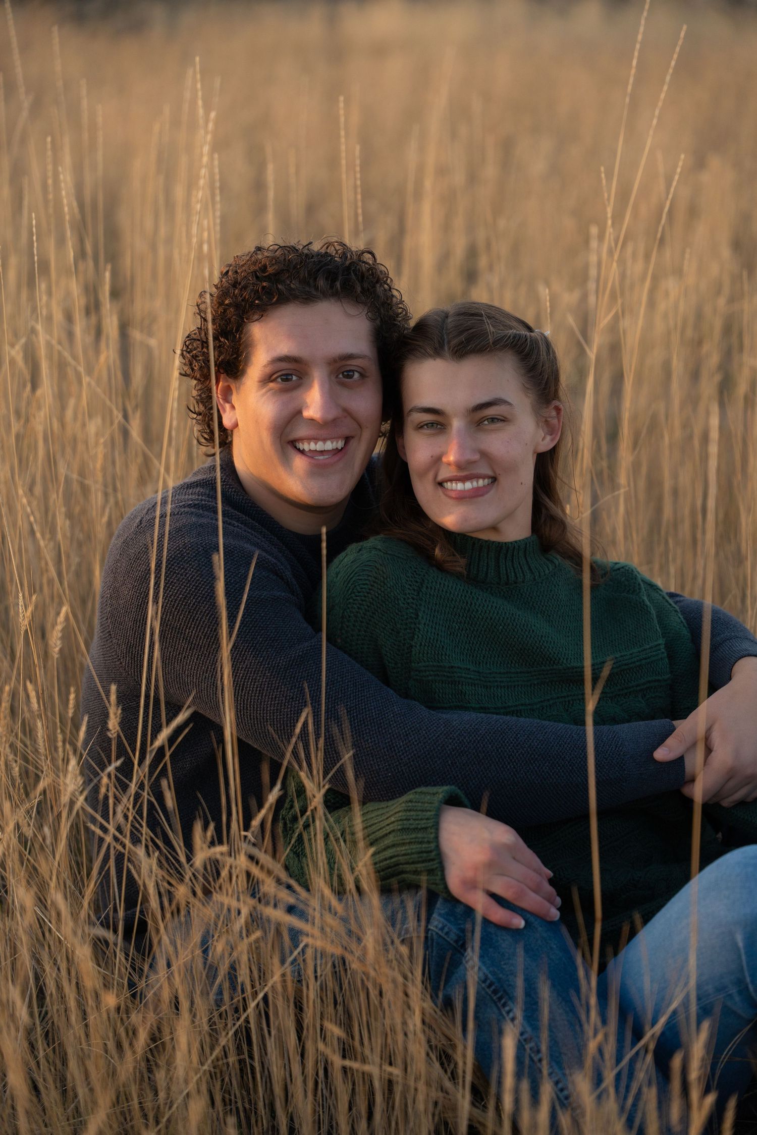 Happy couple sitting together in golden grass during sunset.