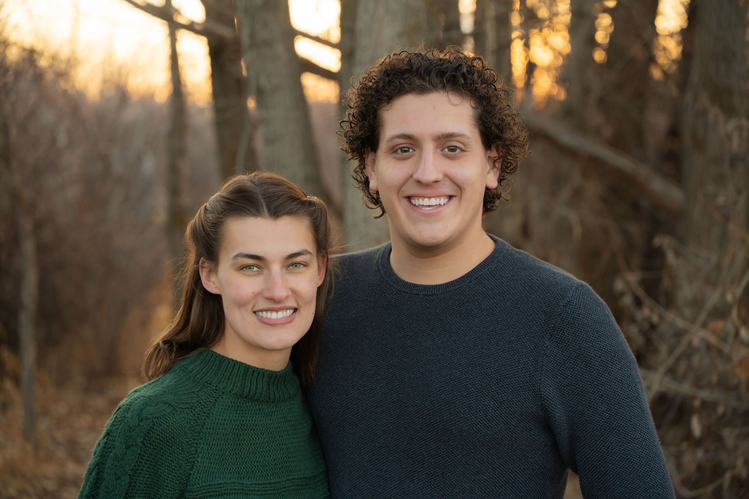 Couple posing together outdoors during golden hour in casual attire.