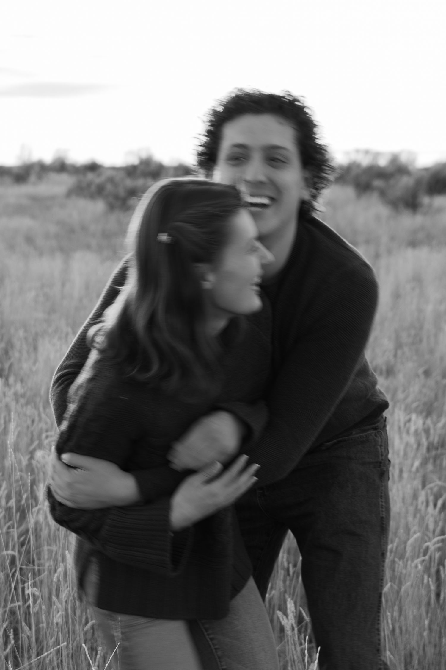Couple embracing in tall grass field during black and white photoshoot.