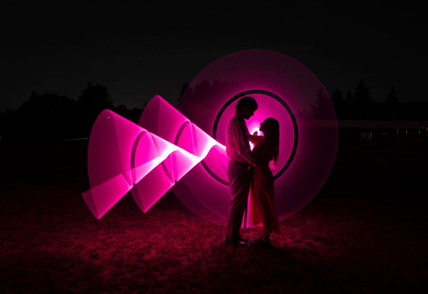 Light painting photography creating glowing pink geometric shapes in darkness.
