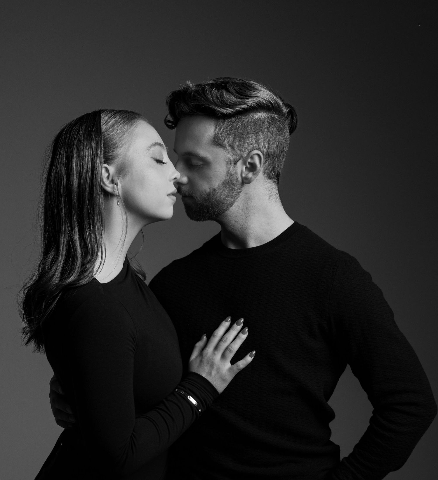 Artistic black and white portrait of a couple in black sweaters sharing an intimate moment.