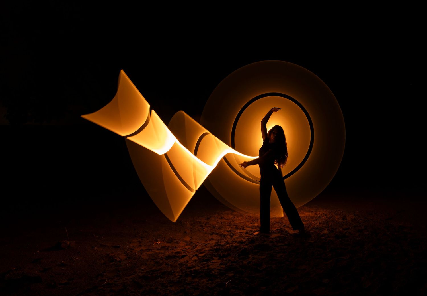 Light painting photography creating warm golden arcs and circles in the darkness.