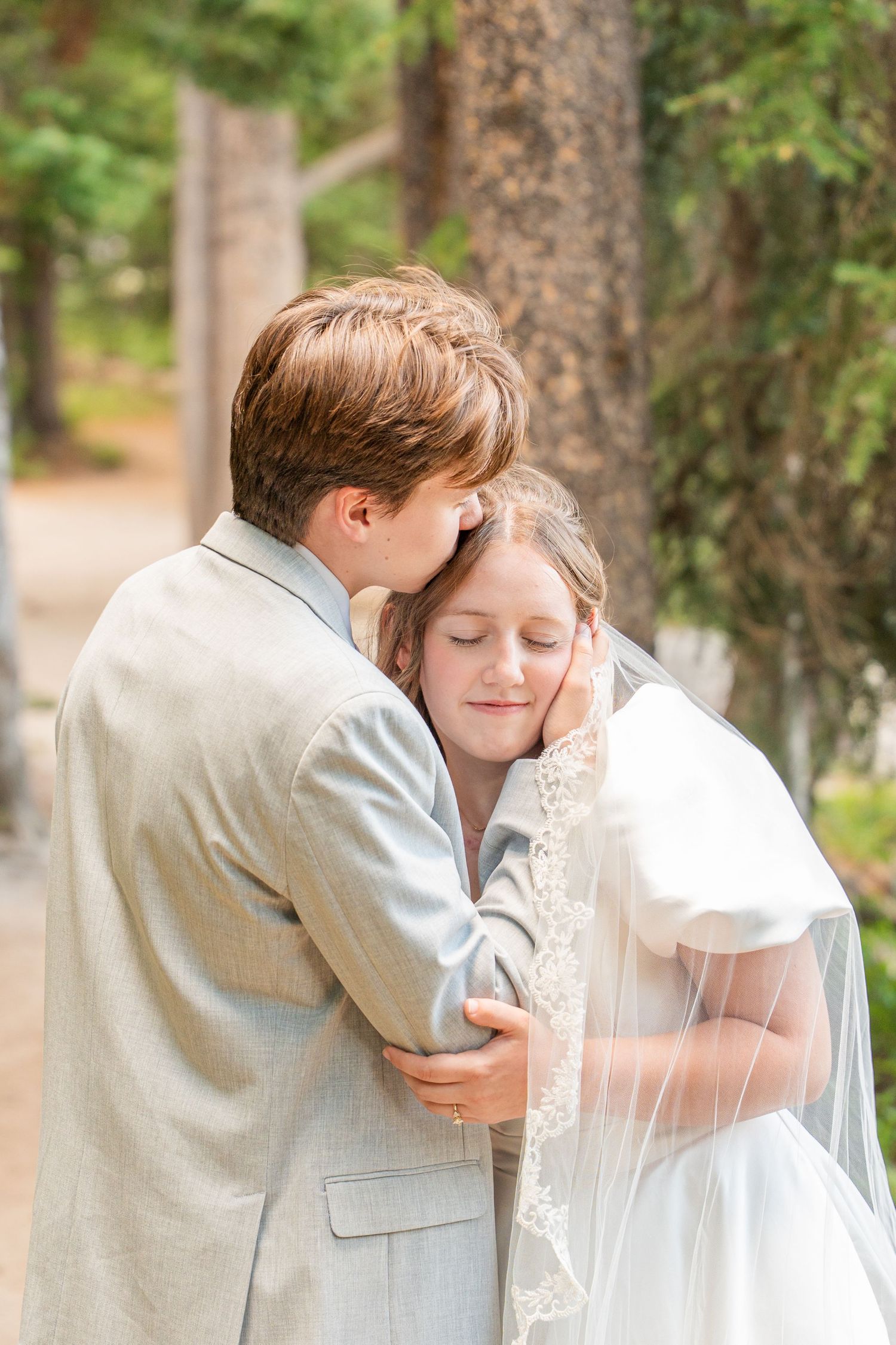 A tender embrace between newlyweds in a wooded forest setting with soft natural light.