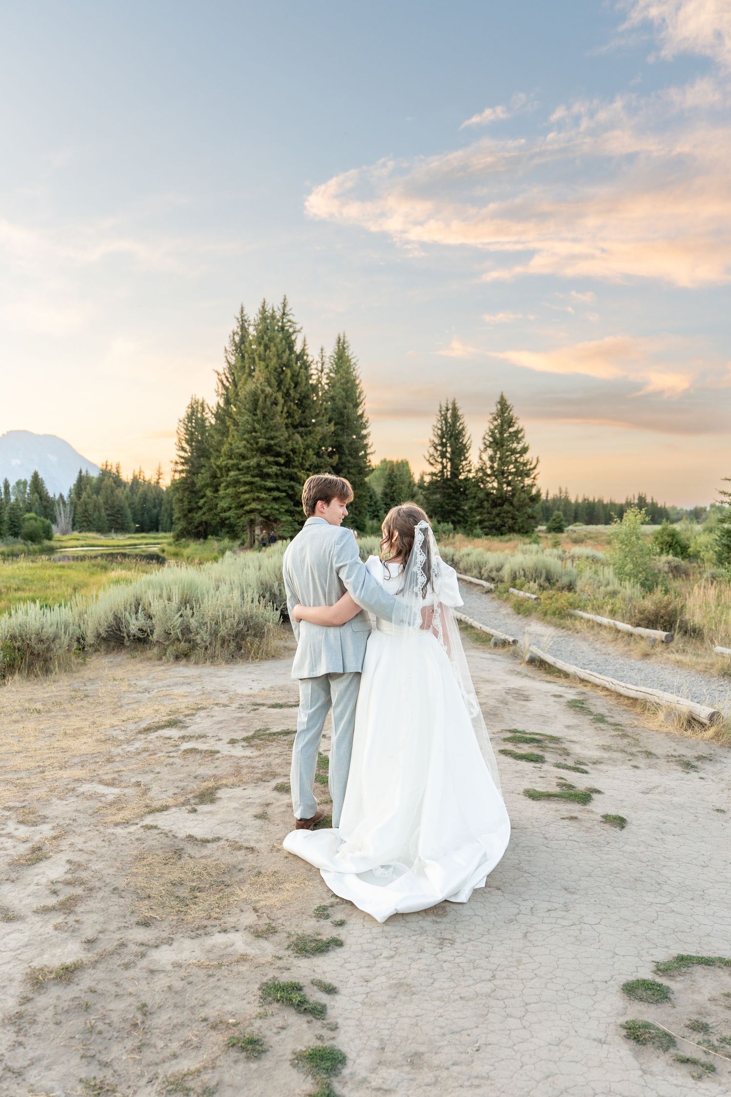 Couple walking along a scenic mountain path at sunset with flowing white dress.