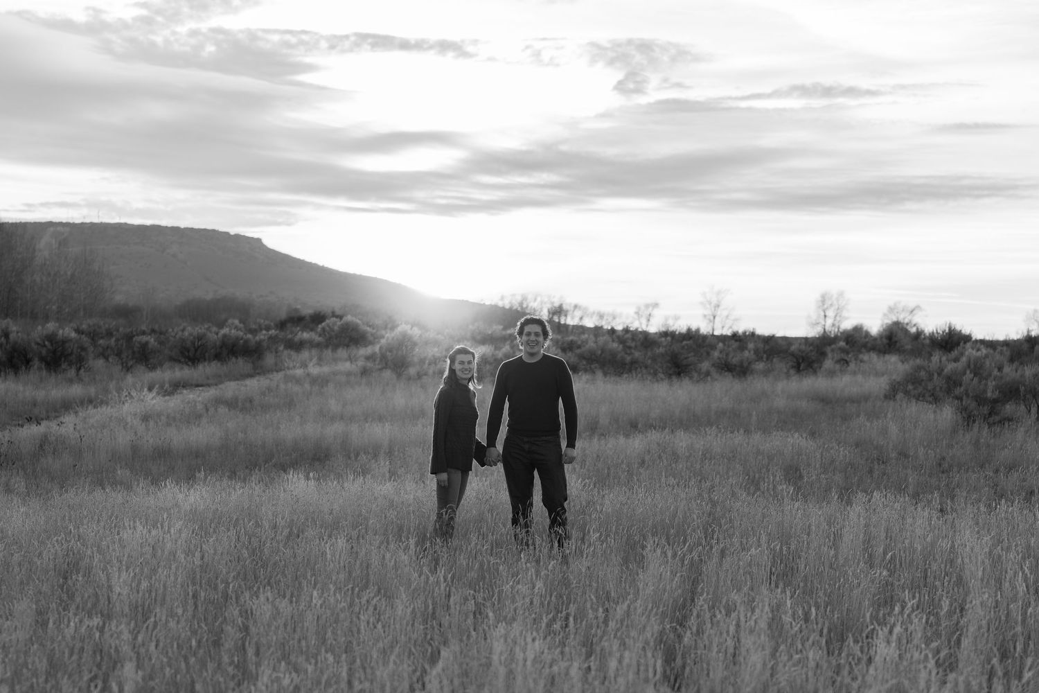 Silhouetted figures walking through grassy field at sunset.
