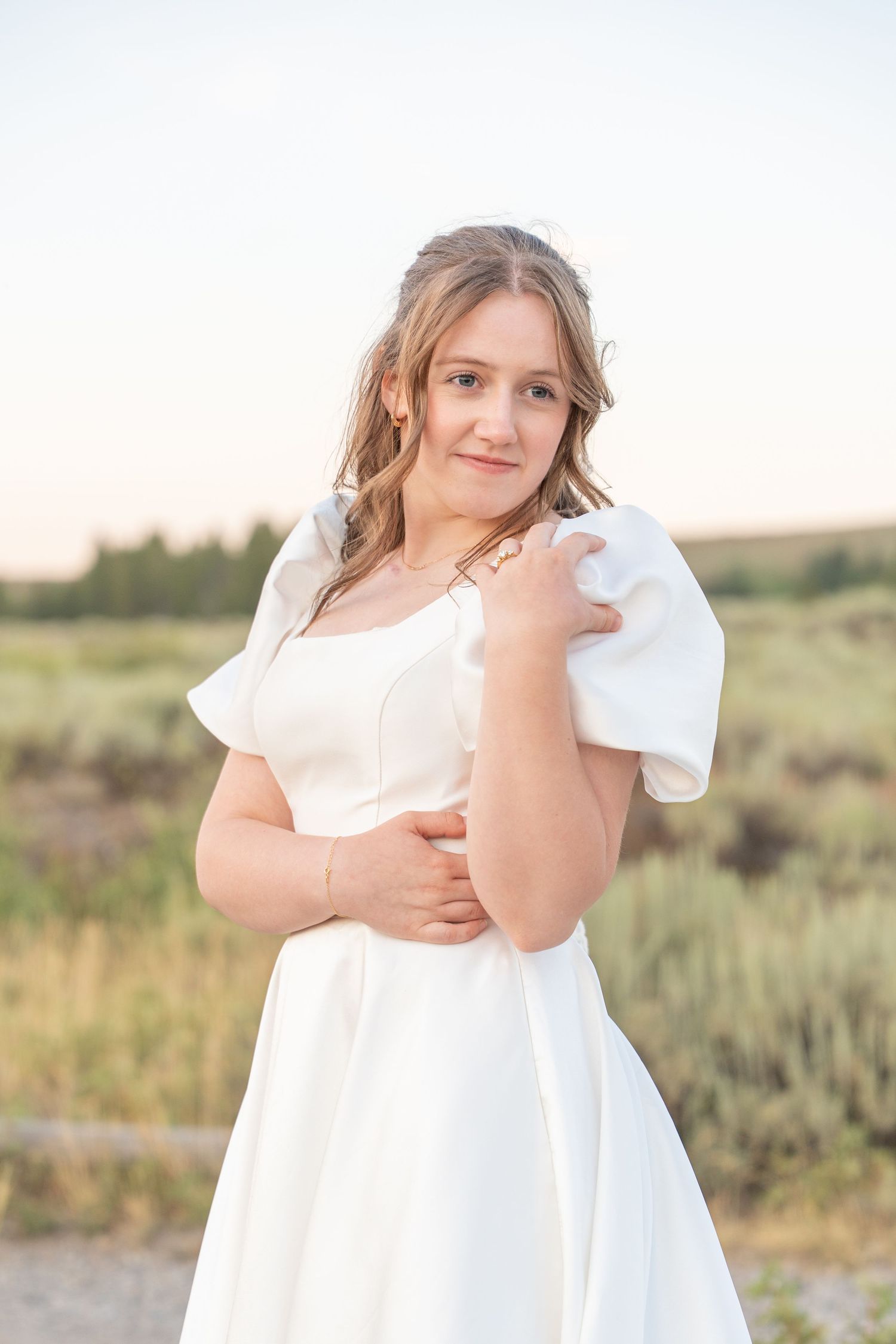 Bride in simple white dress poses in natural outdoor setting at sunset.
