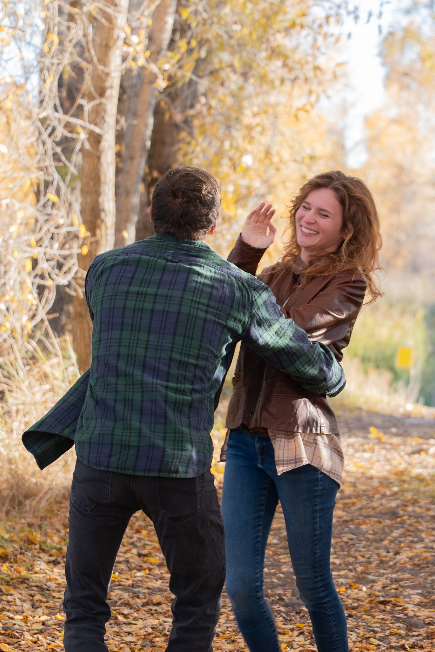 Playful autumn photoshoot with two people dancing among fall trees.