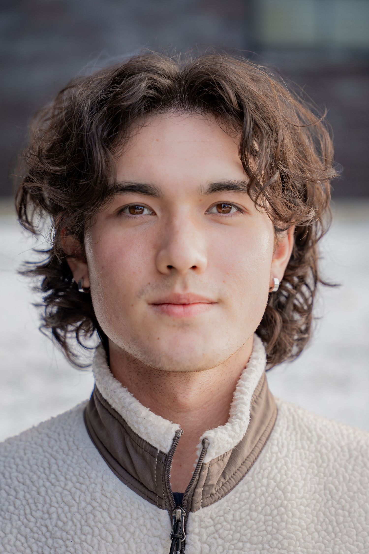 Portrait showing curly brown hair and white winter jacket against snowy background.