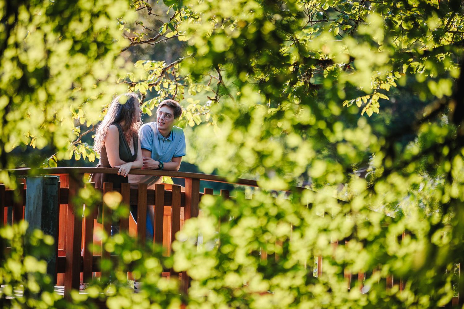 Couple s'enlaçant sur un pont en bois dans un écrin de verdure par Eric Filliat. Photographie de couple au naturel. Pilat, Saint-Étienne