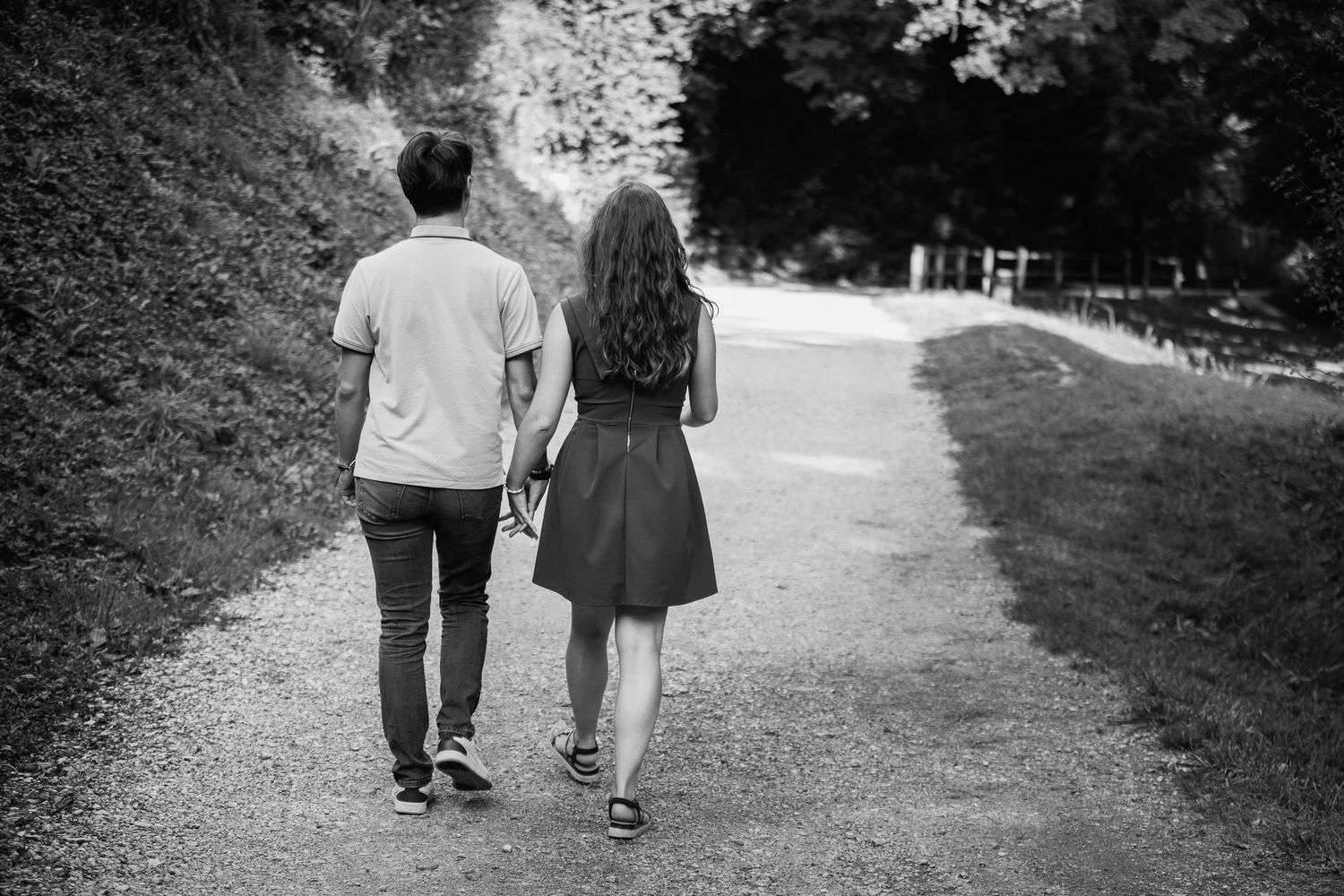 Moment complice d'un couple de mariés marchant sur un chemin de campagne, vue de dos, esthétique noir et blanc. Rhône - Ain