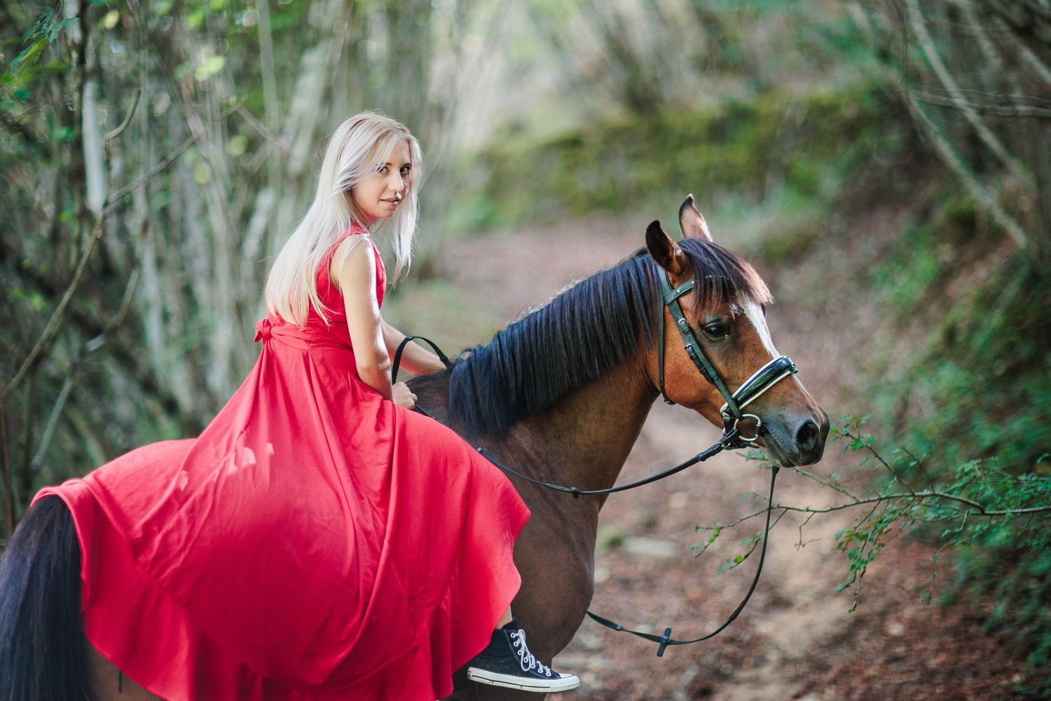 Portrait élégant d'une cavalière en robe rouge et sa jument dans un bois, symbolisant la connexion et l'esthétique entre l'humain & l'animal