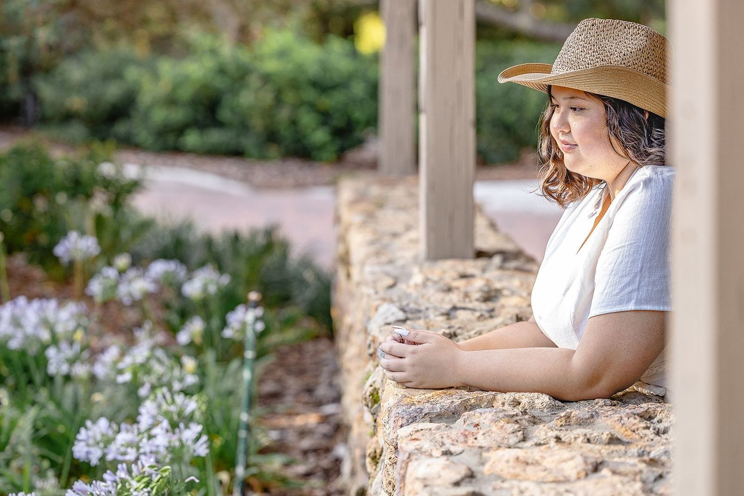 Relaxed outdoor senior portrait surrounded by greenery, sunlight, and peaceful charm.