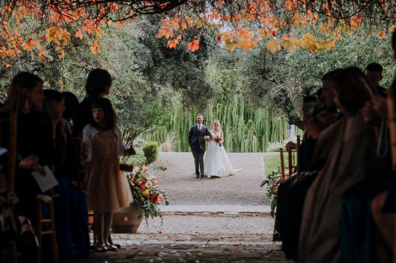 Bride walking down outdoor aisle under colorful floral canopy at garden wedding.