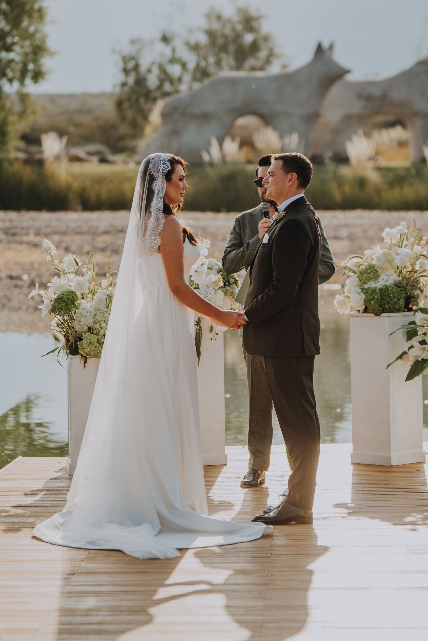 Bride and groom exchanging vows on waterfront dock surrounded by white floral arrangements.