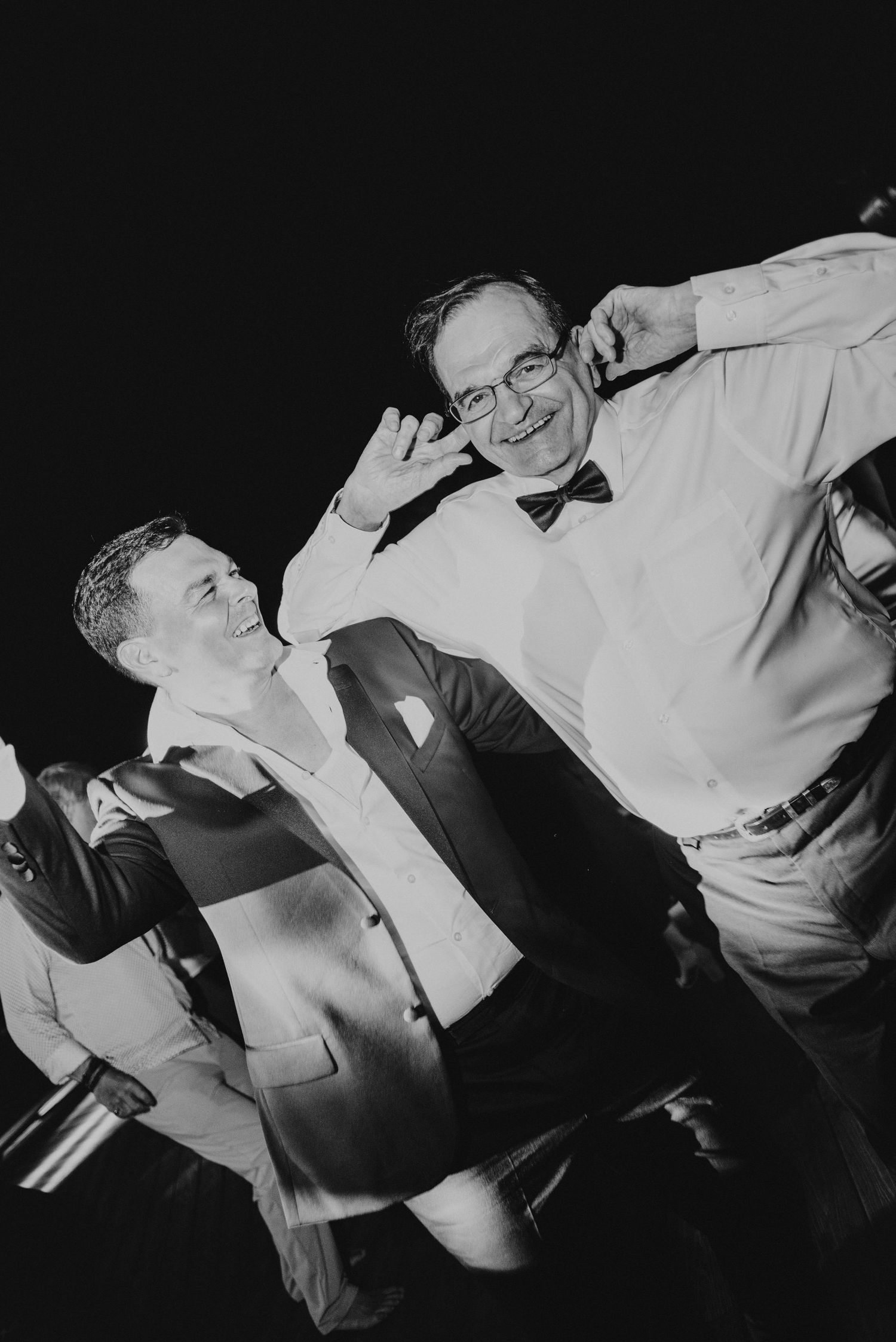 Two men dance and celebrate joyfully at a wedding reception in this fun black and white party photo.