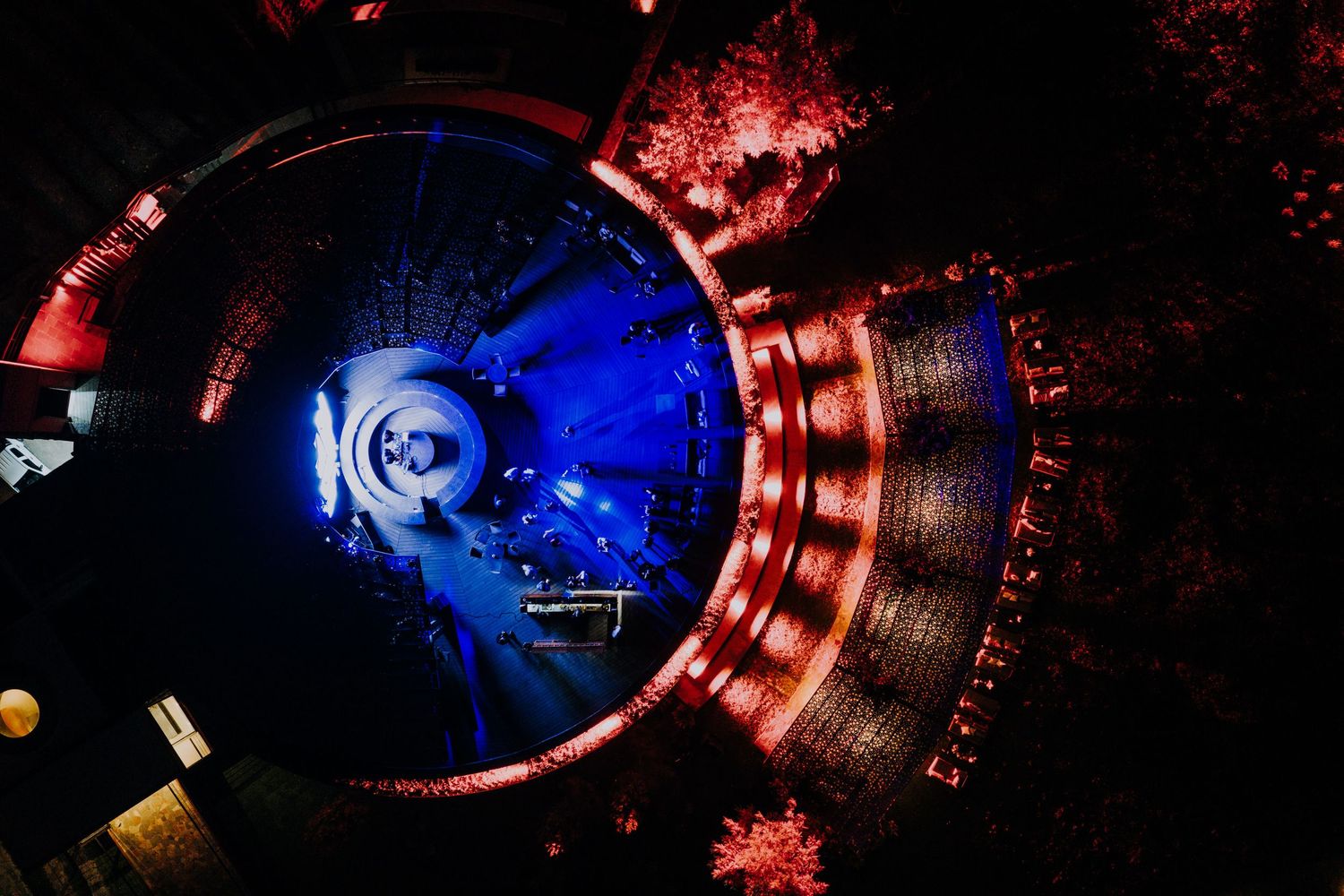 Aerial view of a stunning circular concert stage lit with blue and red dramatic lighting.