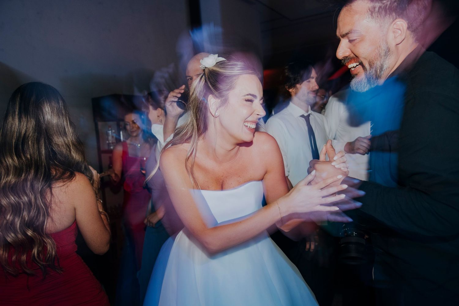 Bride laughs and dances with guests during lively wedding reception dance floor celebration.