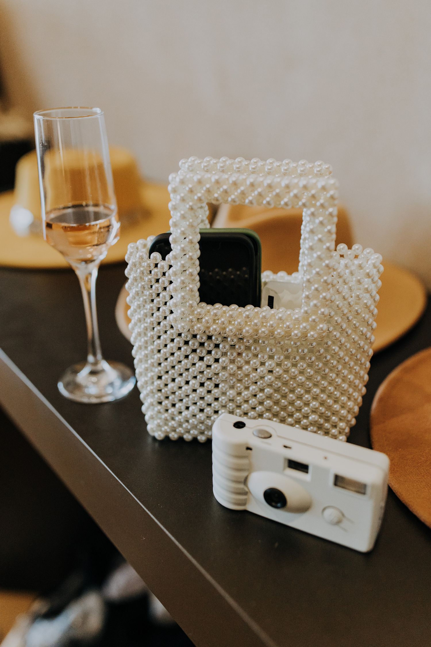 Pearl beaded handbag with disposable camera and champagne flute on dark table.