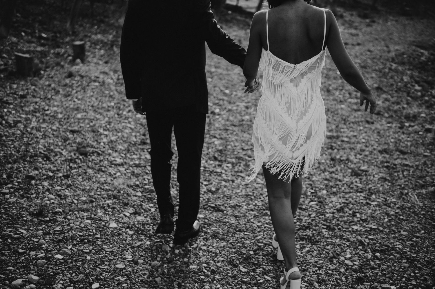 Black and white photo of bride and groom walking hand in hand on gravel path.