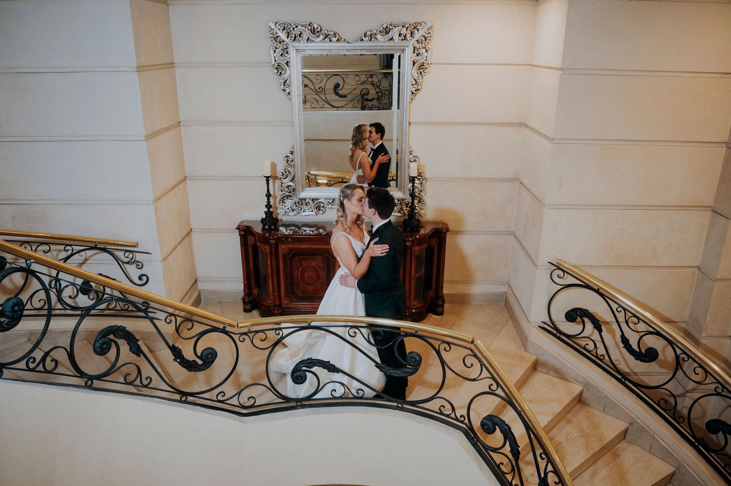 Bride and groom kissing on grand staircase with mirror backdrop.