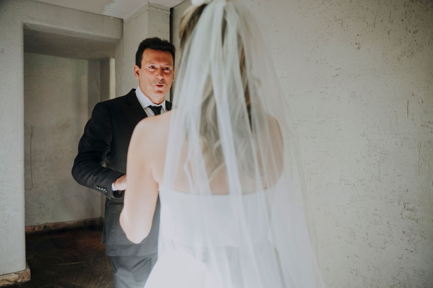 Groom in dark suit seeing bride in white veil and dress for the first time at wedding first look moment.