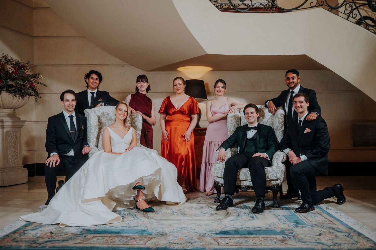 Wedding party group portrait with bride and groom seated in elegant venue.