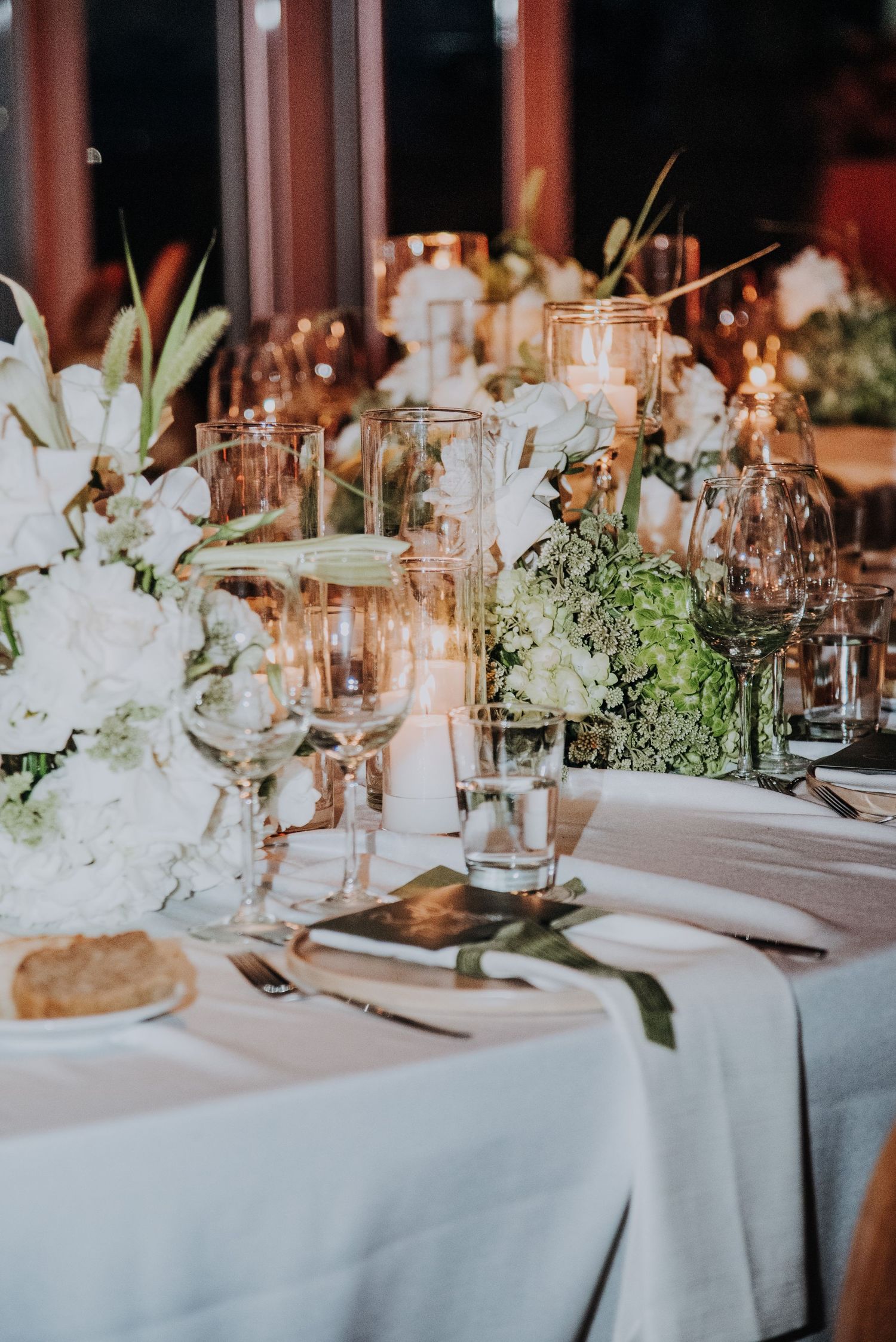 Romantic wedding reception table with white floral centerpieces, candles, and crystal glassware.