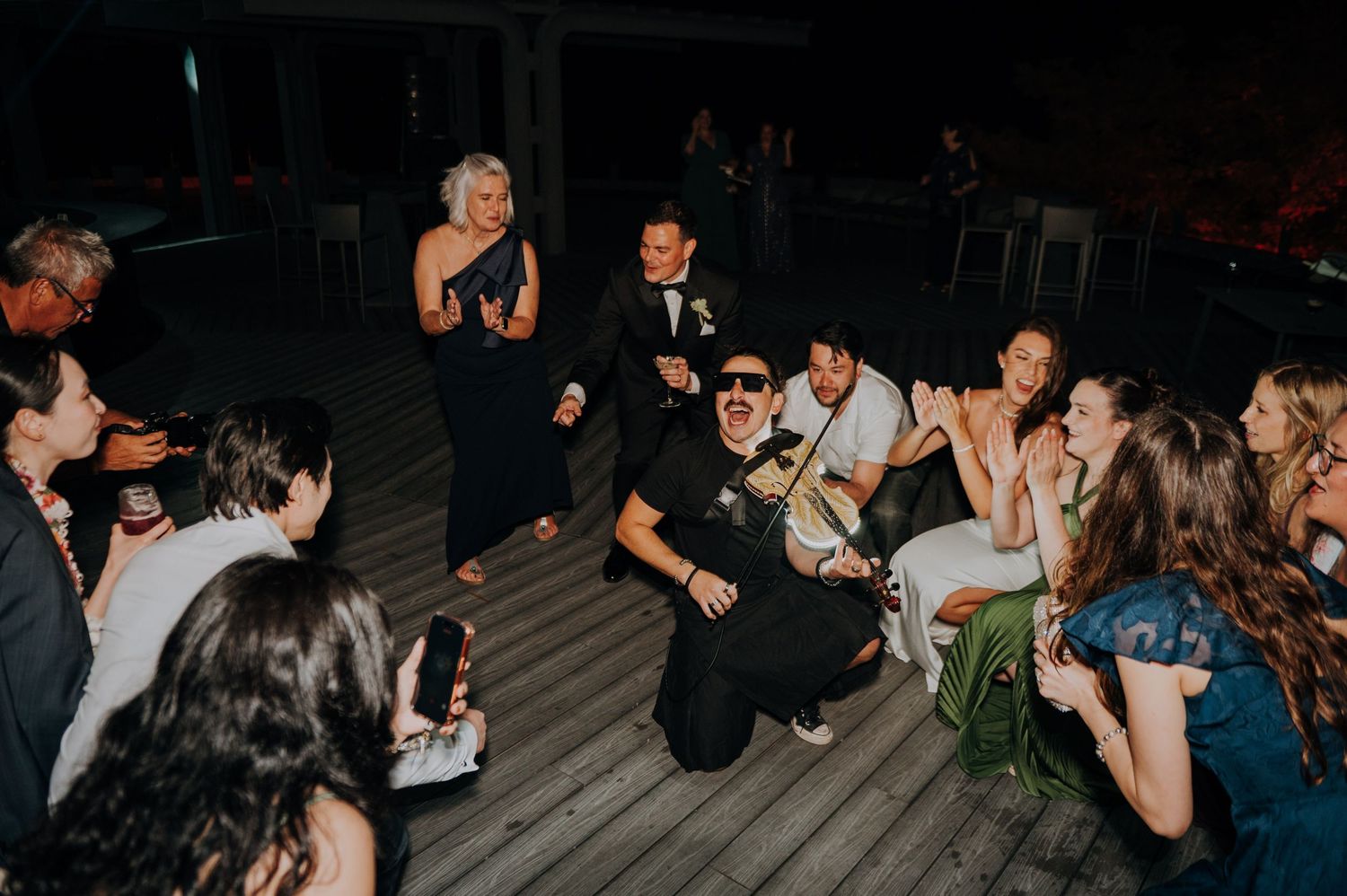 Wedding guests gathered on a deck at night celebrating and dancing during a lively outdoor reception party.