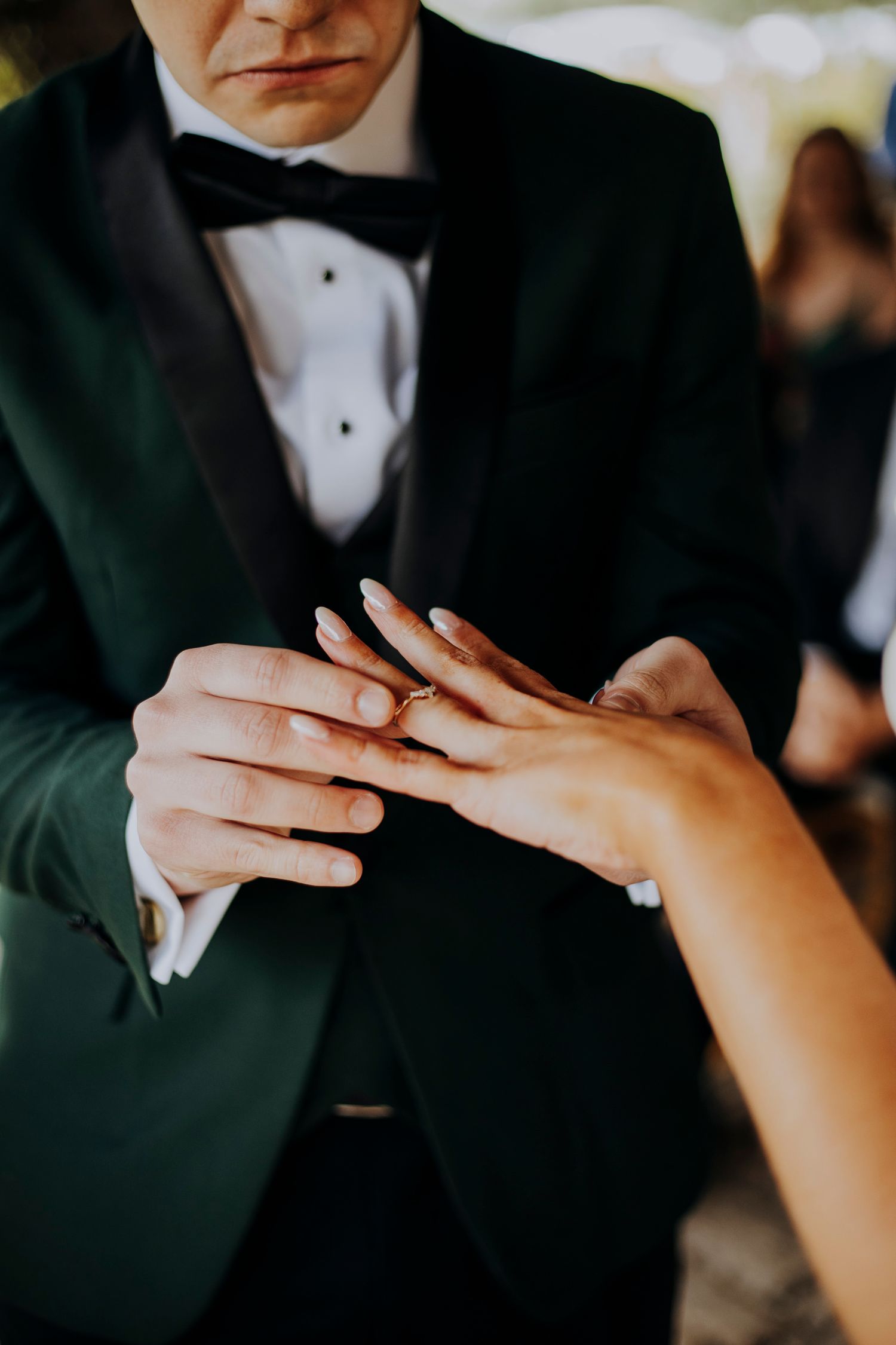 Groom in green tuxedo placing gold wedding ring on brides hand during ceremony.
