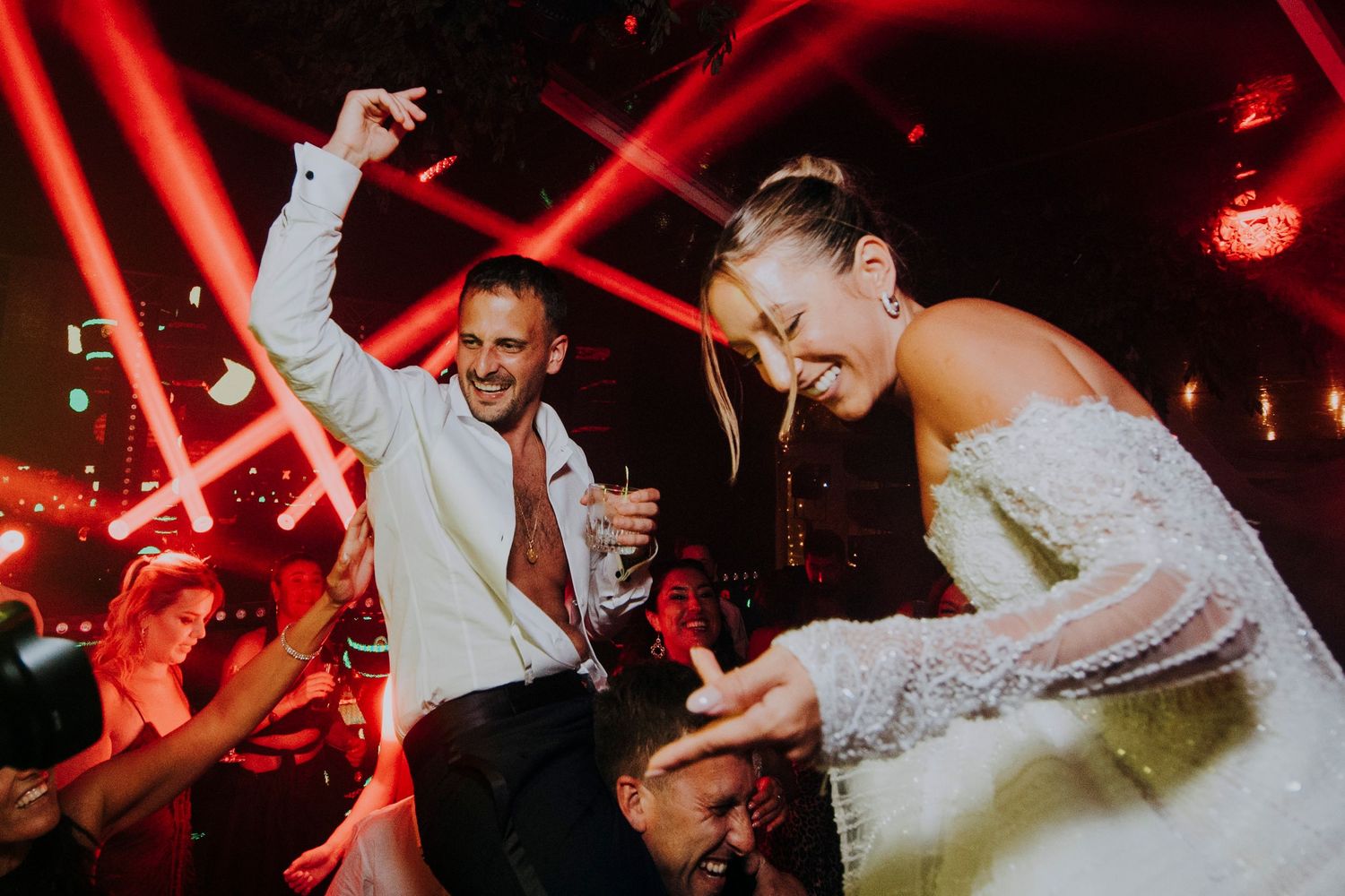 Bride and groom dance energetically under red laser lights at their lively wedding reception party.