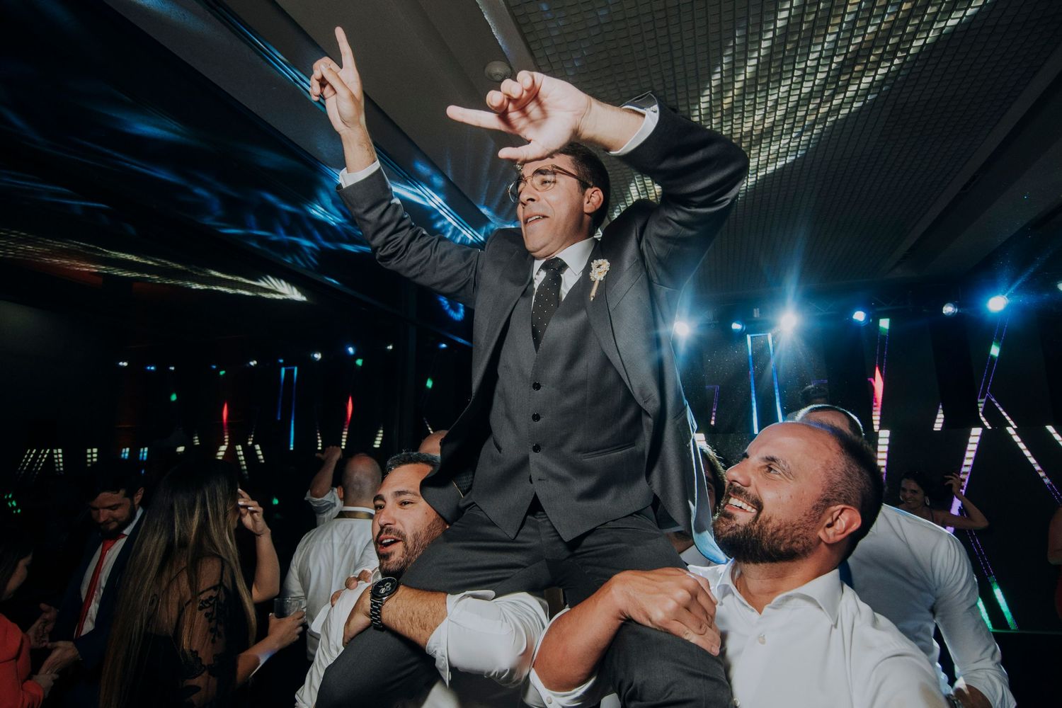 Groom lifted on shoulders by groomsmen celebrating on the dance floor at a lively wedding reception.