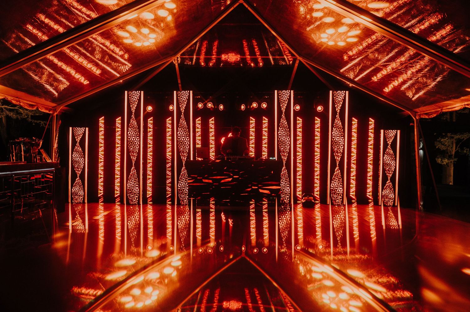 Dramatic red-lit wedding dance floor with decorative light columns inside tent venue.