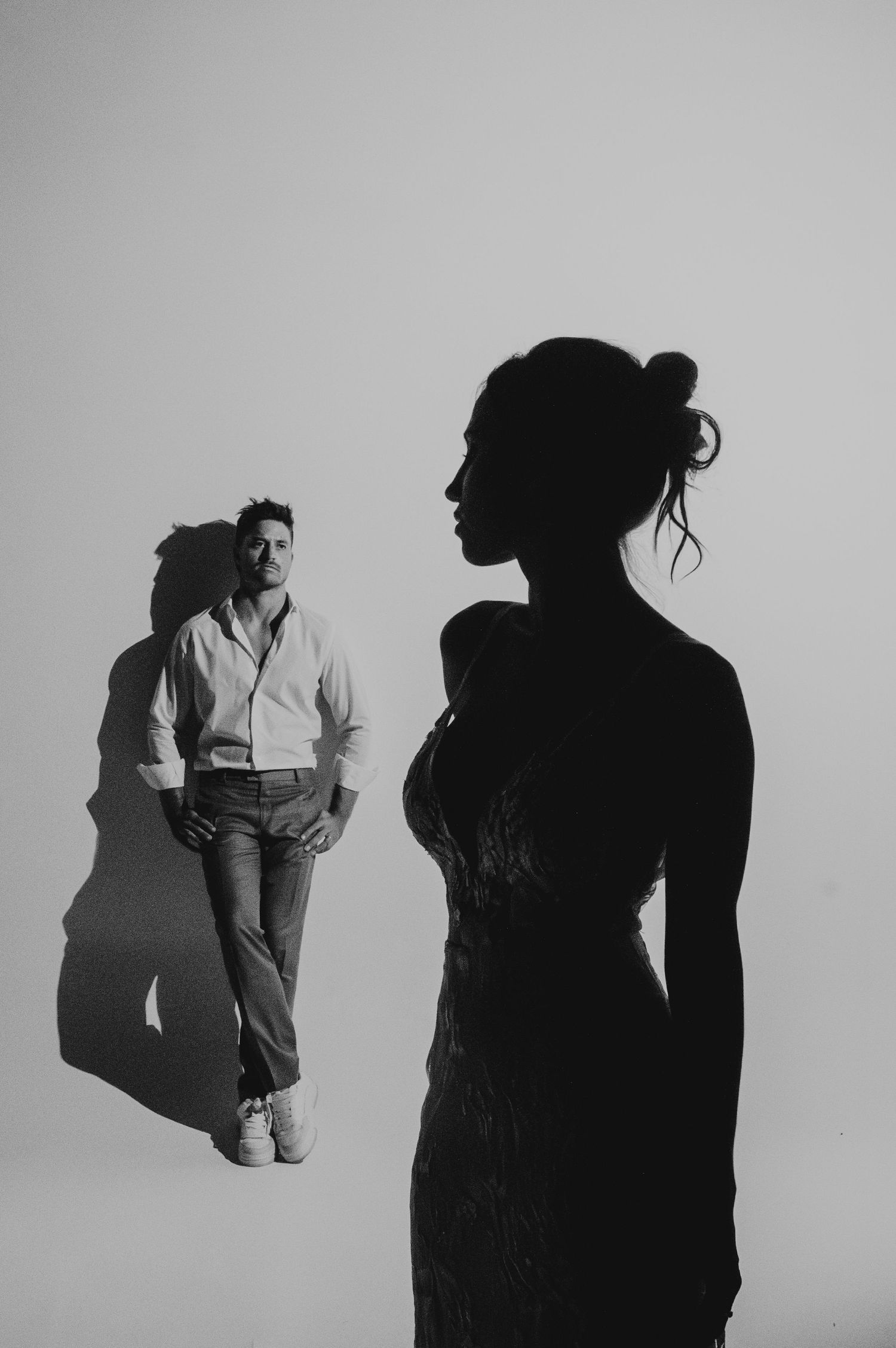 Artistic black and white portrait of couple, woman silhouetted in foreground, man leaning on wall. Couple portrait in Mendoza.