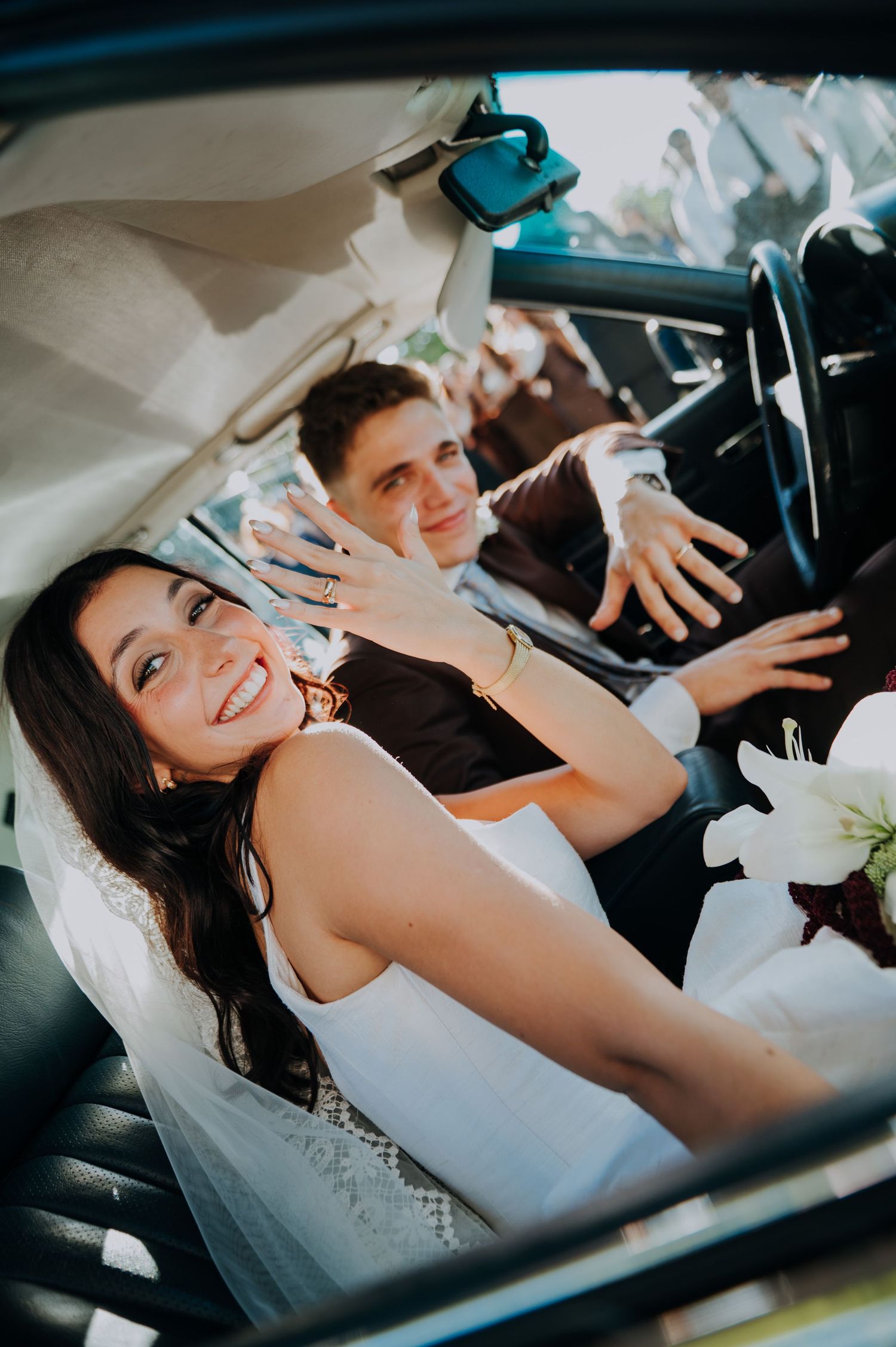 Smiling bride shows wedding ring while sitting with groom in vintage convertible car. wedding photographer in mendoza