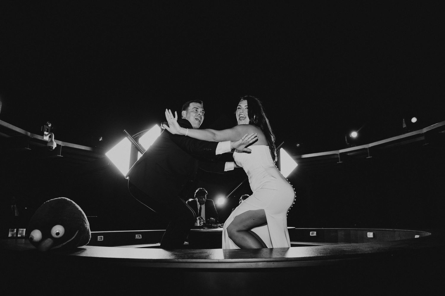 Black and white photo of couple dancing dramatically on stage under spotlights at wedding reception.