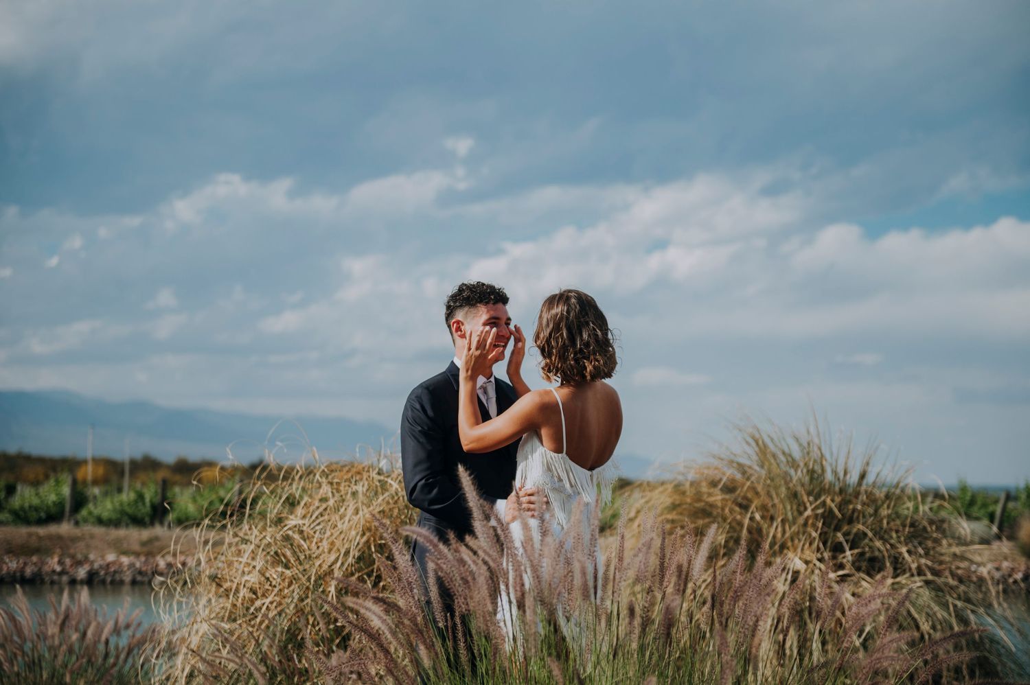 Groom tenderly holds brides face in a romantic outdoor portrait among tall golden grasses.