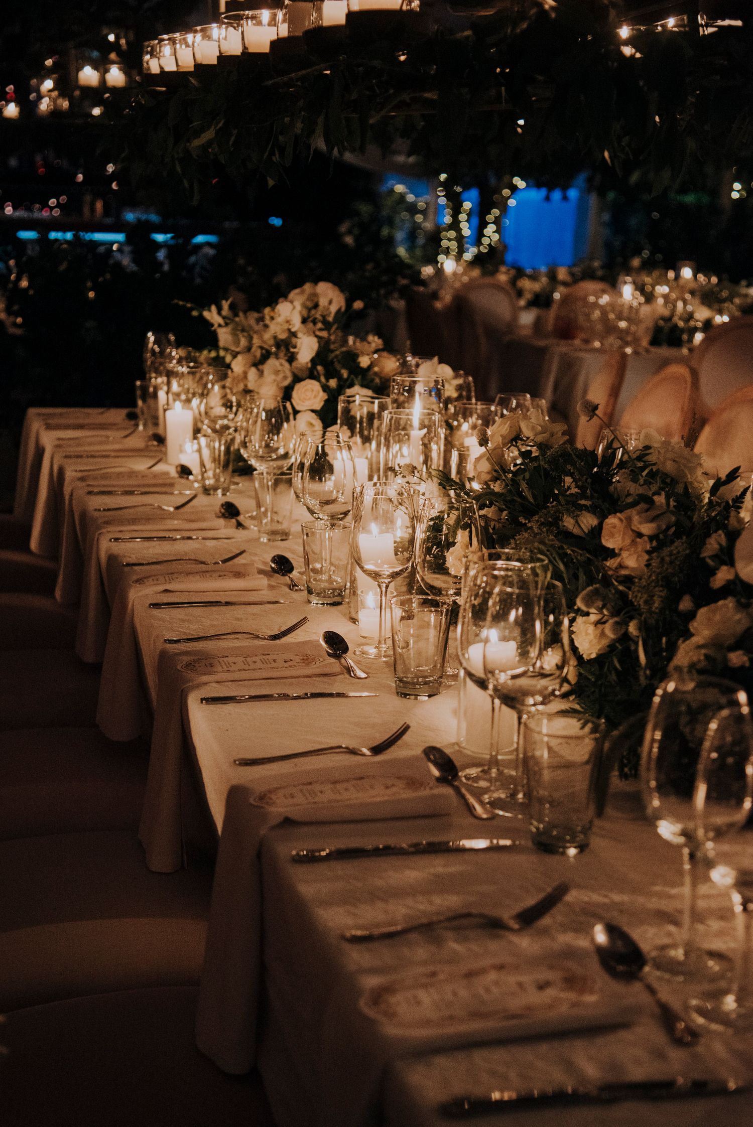 Candlelit wedding reception table with white floral arrangements and crystal glassware.