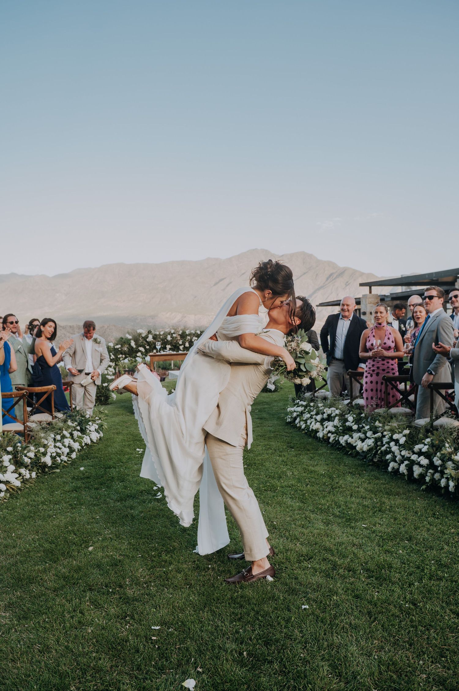 Groom lifting bride for a kiss while walking down the aisle at outdoor wedding ceremony.
