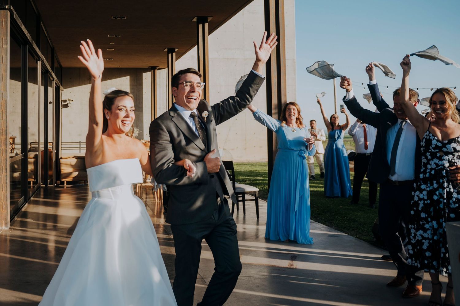 Joyful bride and groom make grand entrance at wedding reception as guests celebrate with raised hands.