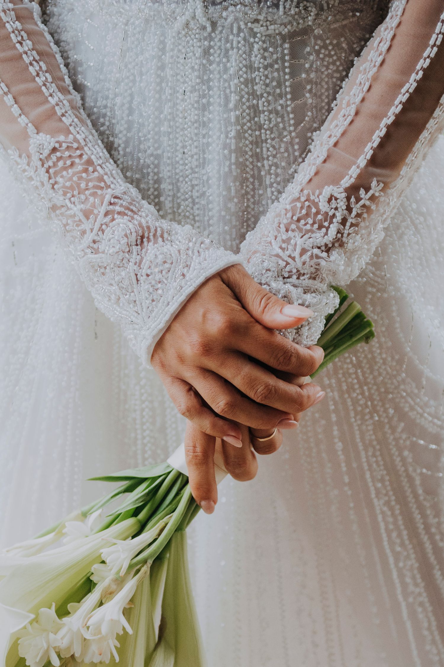 Close-up of bride holding white calla lily bouquet in lace long-sleeve pearl-embellished wedding dress.