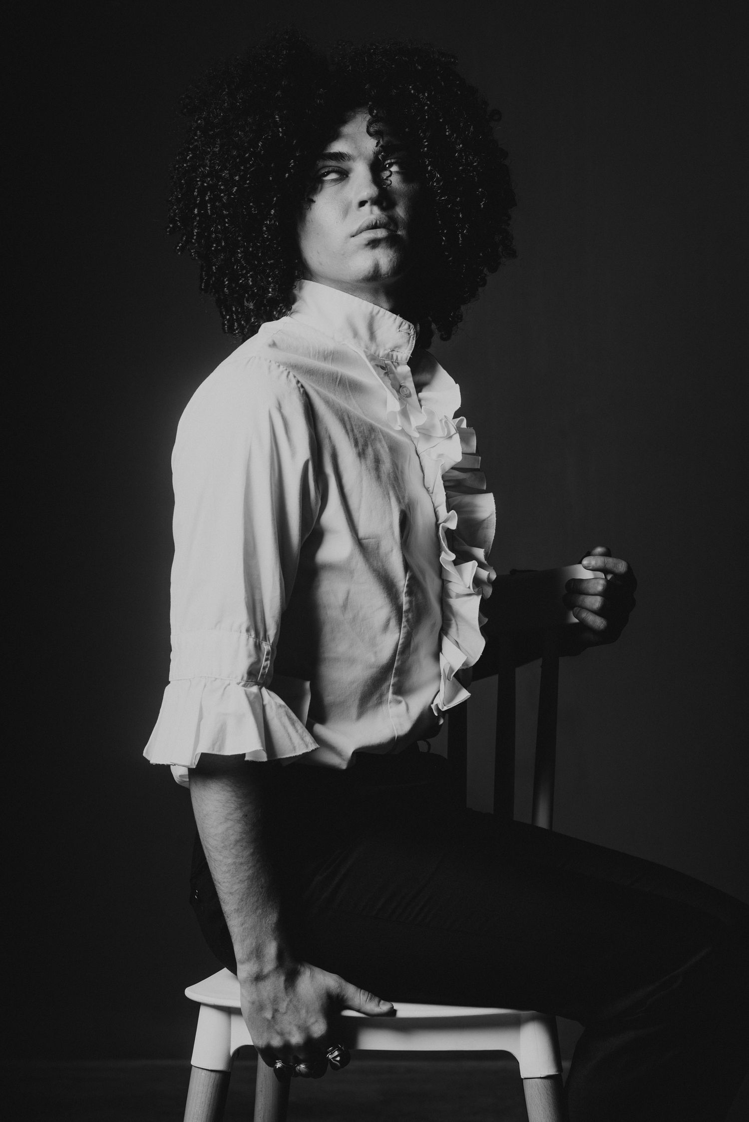 Black and white portrait of a person with curly afro hair in a ruffled shirt.