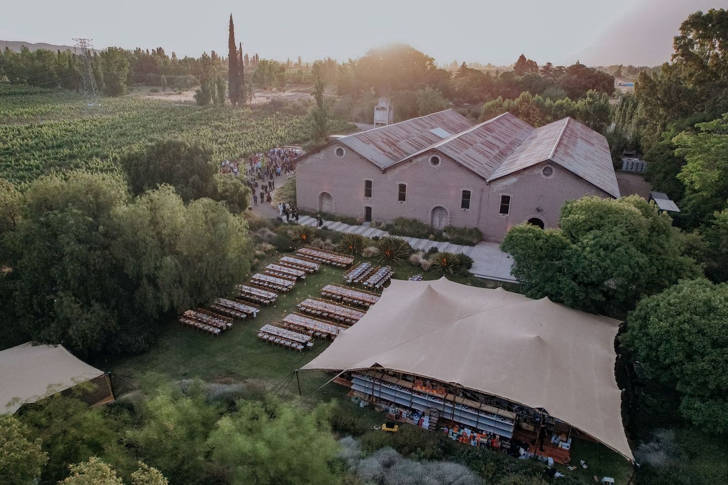 Aerial view of a rustic winery venue with outdoor seating and tent at golden hour sunset.
