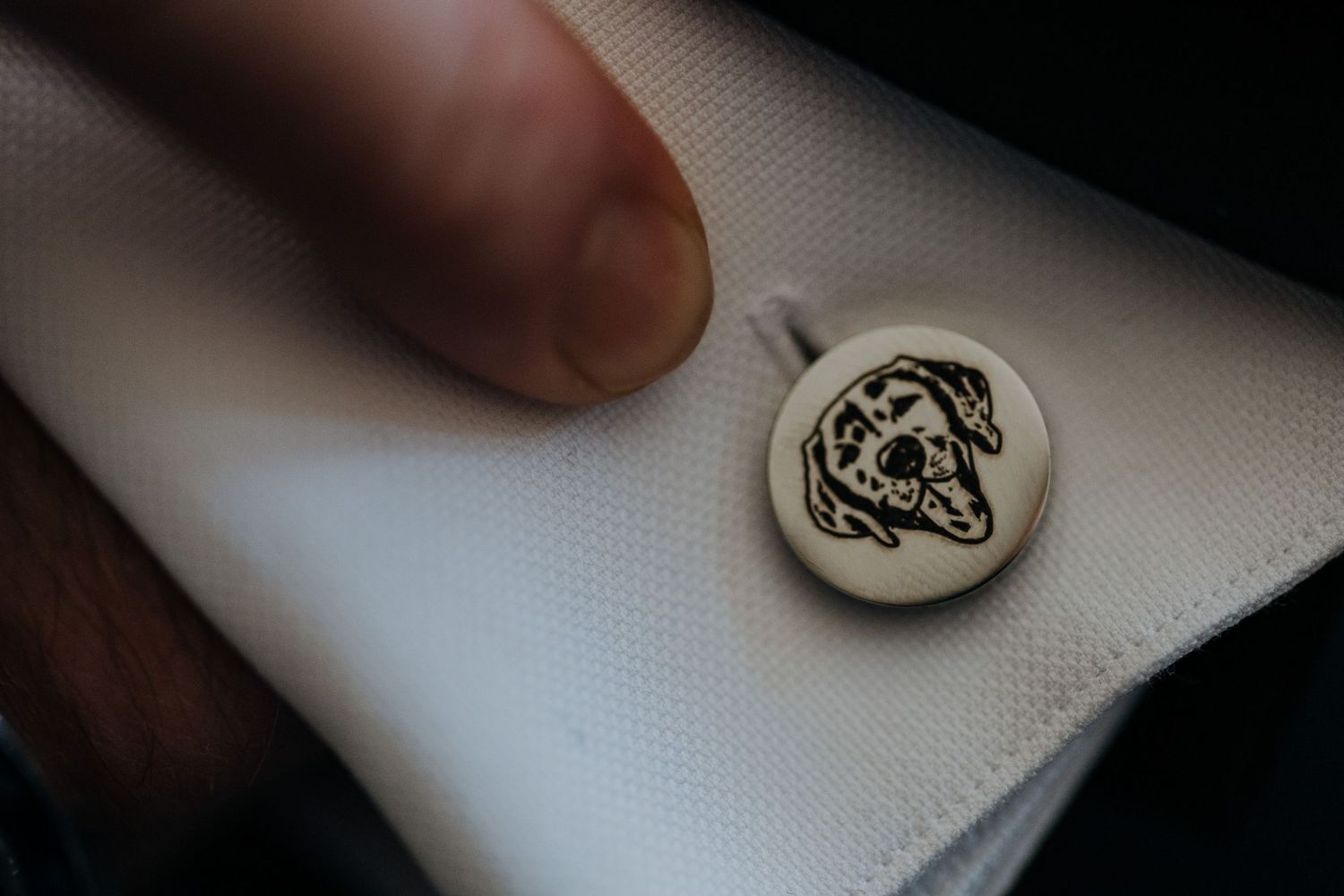 Close-up of an elegant golden cufflink engraved with a dog portrait on a white dress shirt sleeve.