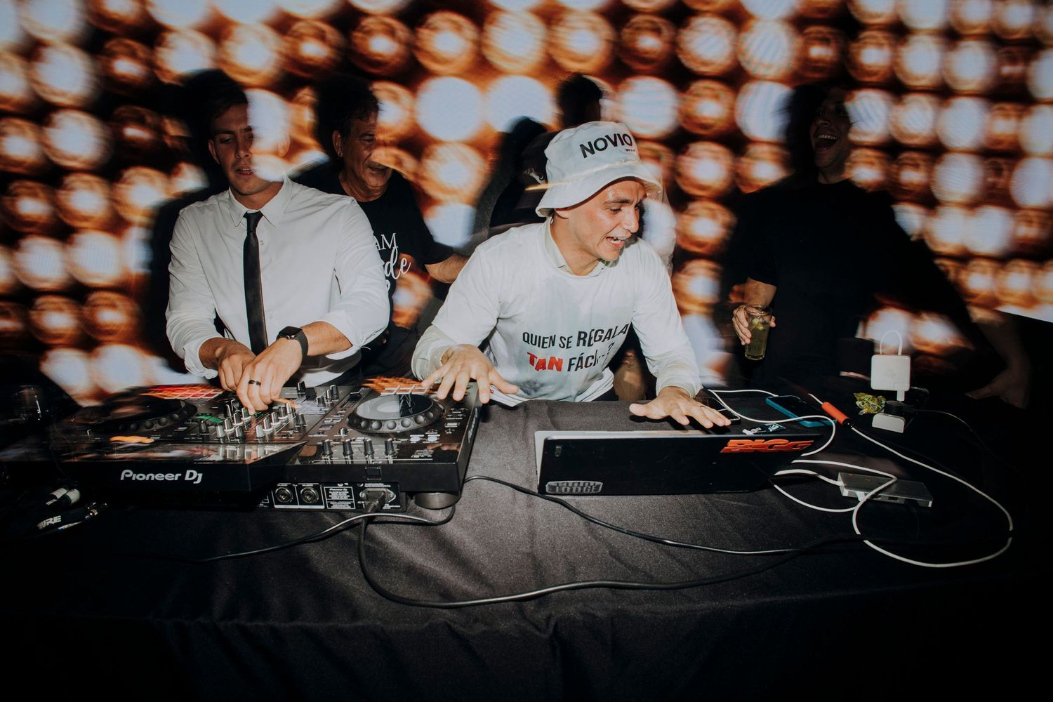 DJ performs at a wedding reception behind Pioneer DJ equipment in front of a glowing light wall.