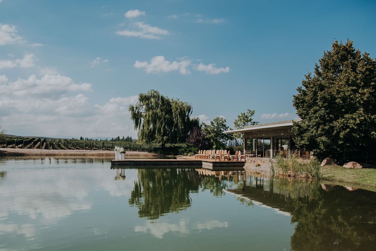 Scenic winery venue with a tranquil pond reflecting blue skies, trees, and an outdoor pavilion.