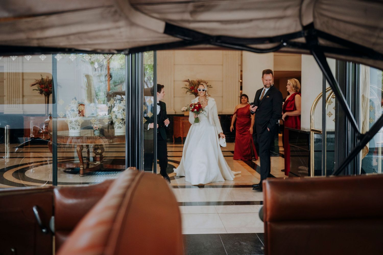 Bride in white gown walks through elegant hotel lobby with escort during wedding day processional.