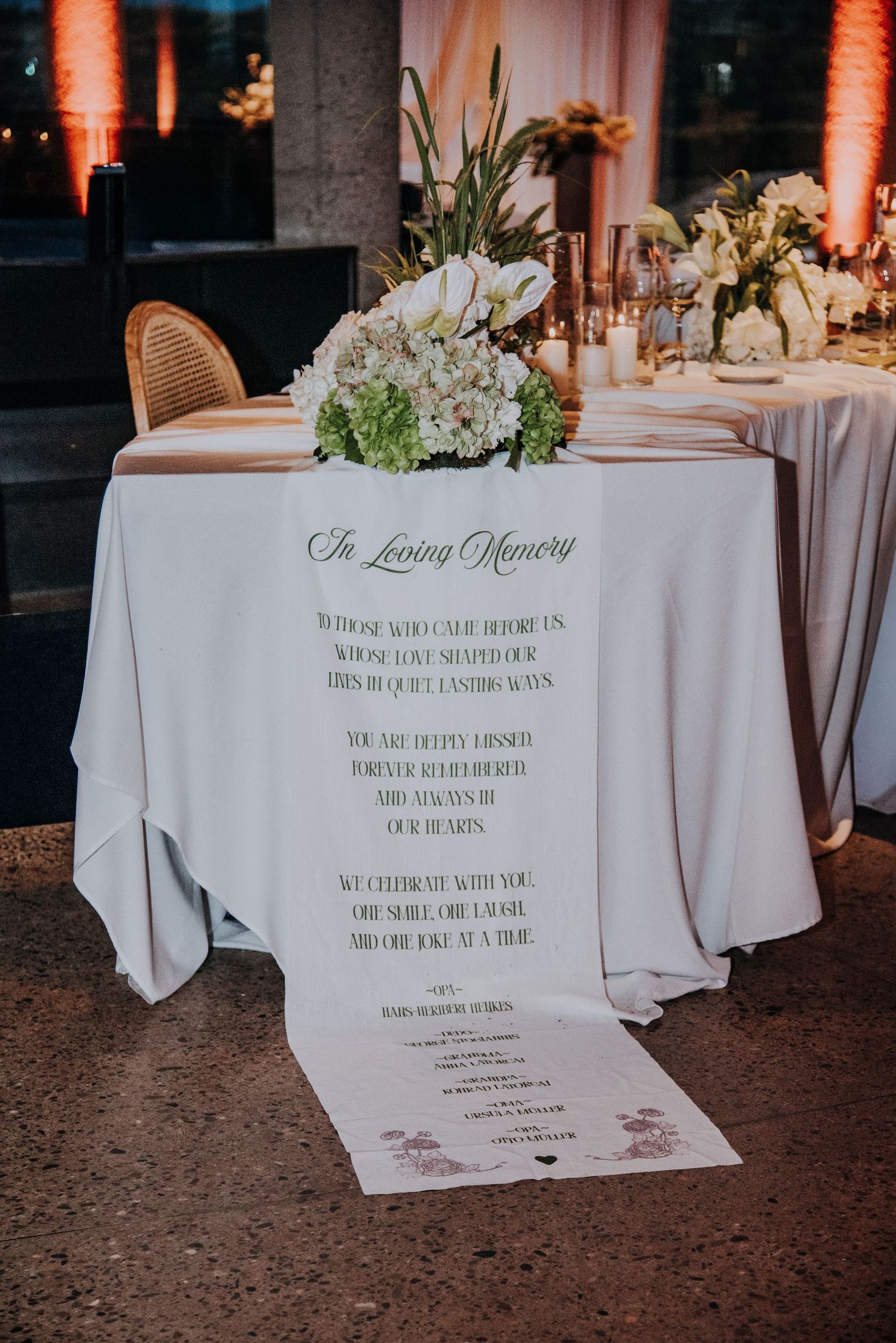 An elegant In Loving Memory wedding table display with white floral arrangements and a printed tribute runner.